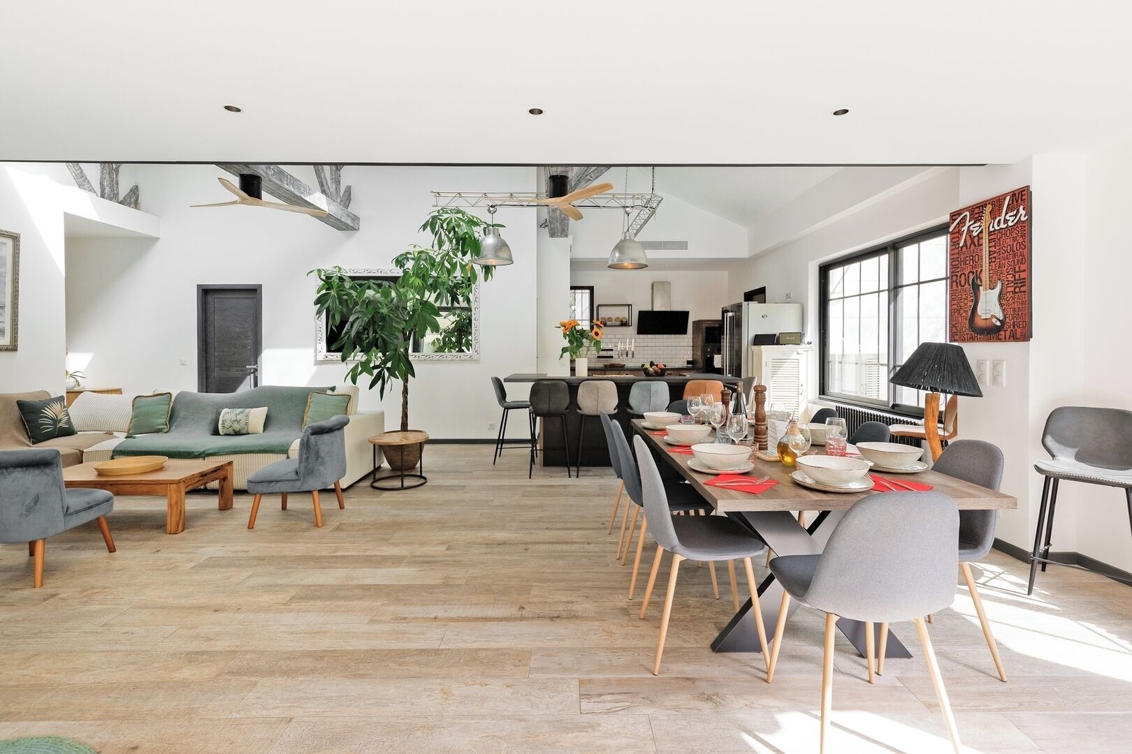 Un salon moderne avec un canapé, des fauteuils, une table à manger dressée pour six personnes et une cuisine en arrière-plan.