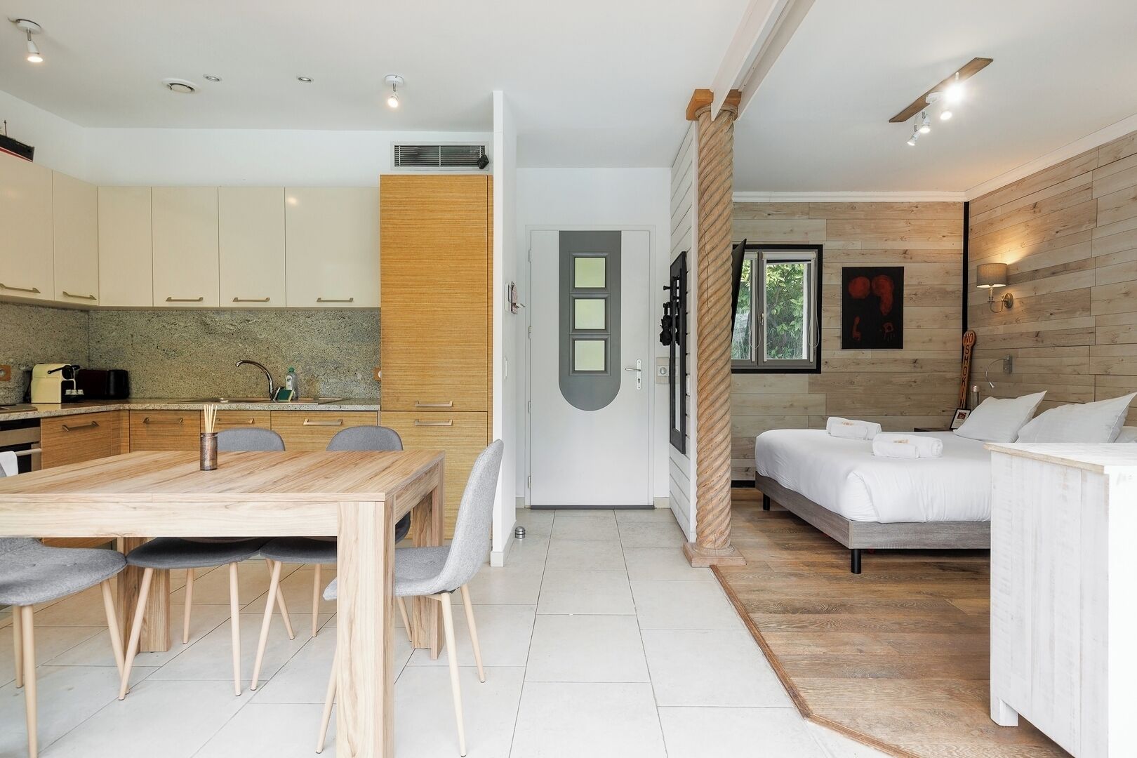 A modern kitchen with a dining area, a sofa, and a bed in a well-lit room with wooden accents.