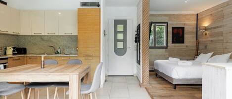 A modern kitchen with a dining area, a sofa, and a bed in a well-lit room with wooden accents.