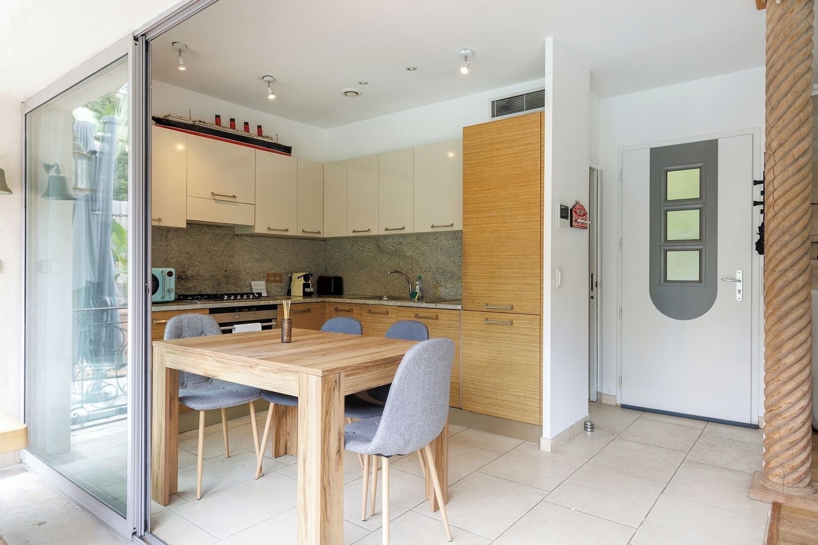 Una cocina moderna con armarios blancos, un muro decorativo de madera y una zona de comedor con mesa y sillas de madera.