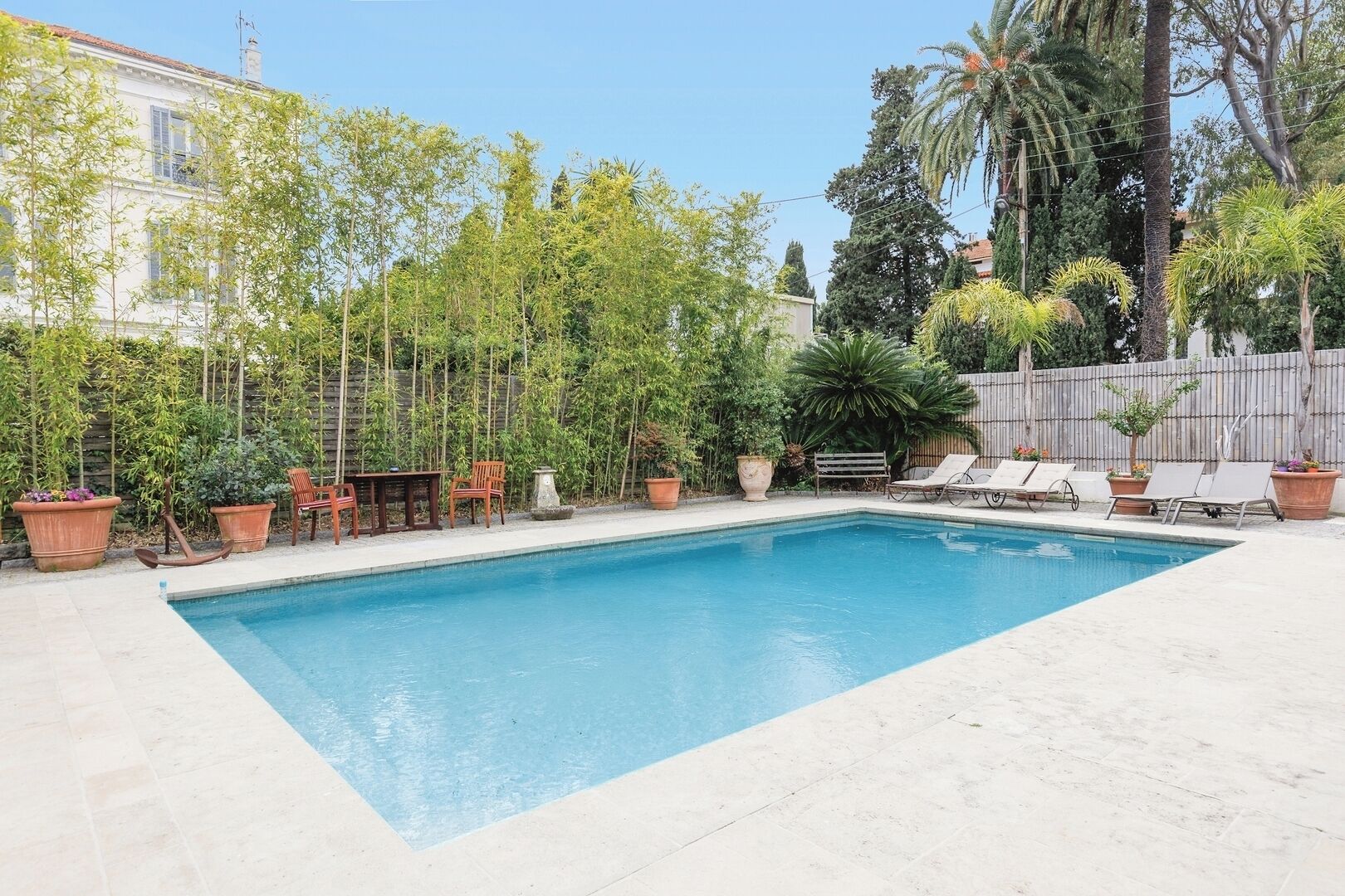 Une piscine rectangulaire avec une terrasse carrelée, entourée de plantes en pot et de mobilier d’extérieur.