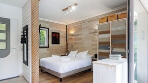 A modern bedroom with a wooden wall panel, a bed with white linens, a bedside table, and a large mirror. - Upstays Pool 200m² Villa Near Beach (Cannes)