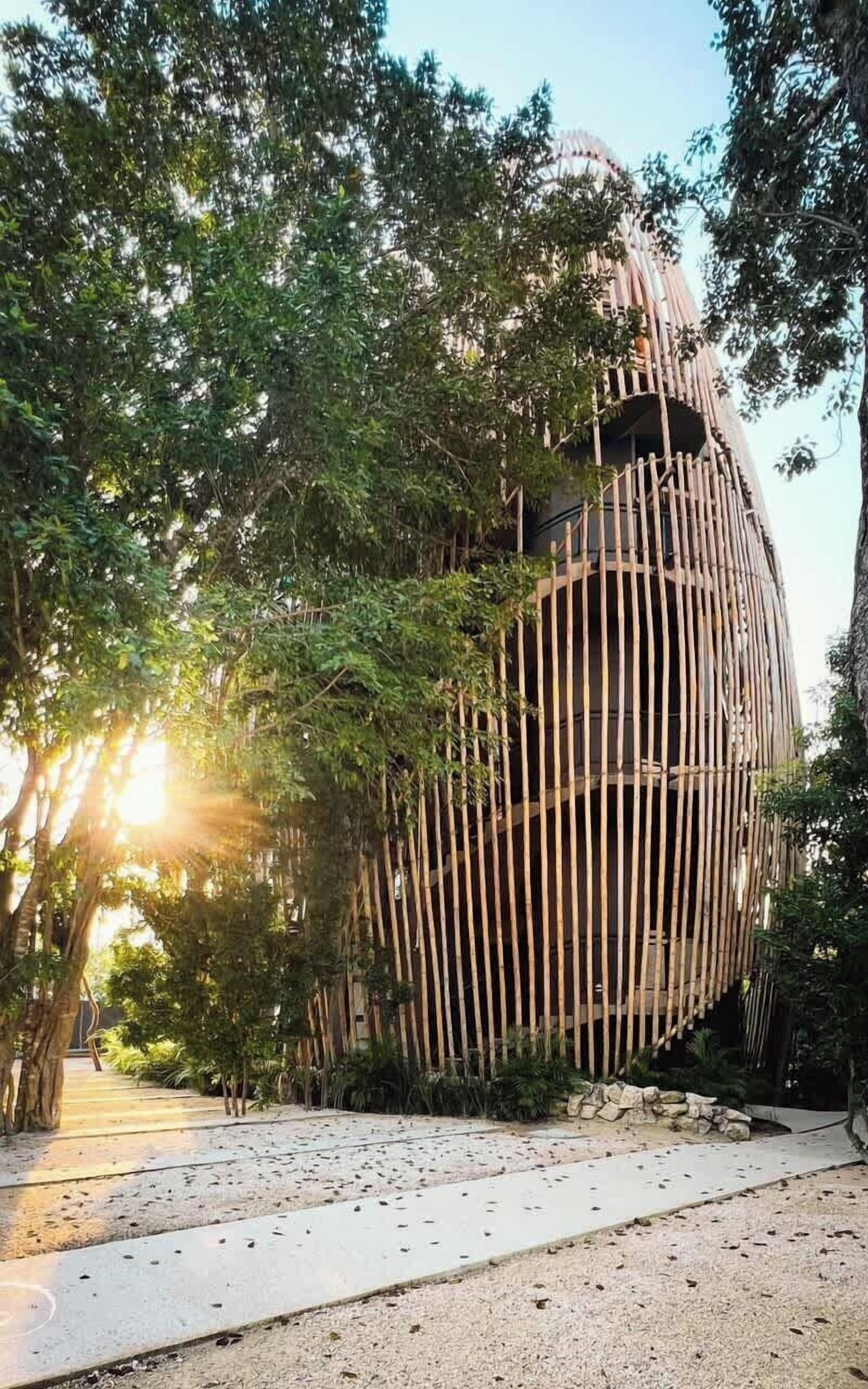 A spherical structure with vertical bamboo elements, surrounded by dense foliage.