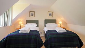 Een slaapkamer met twee bedden, elk met een groene hoofdbord en een ruitdessin deken. Er zijn twee bedlampen, een plafondlamp en twee ingelijste foto's aan de muur.