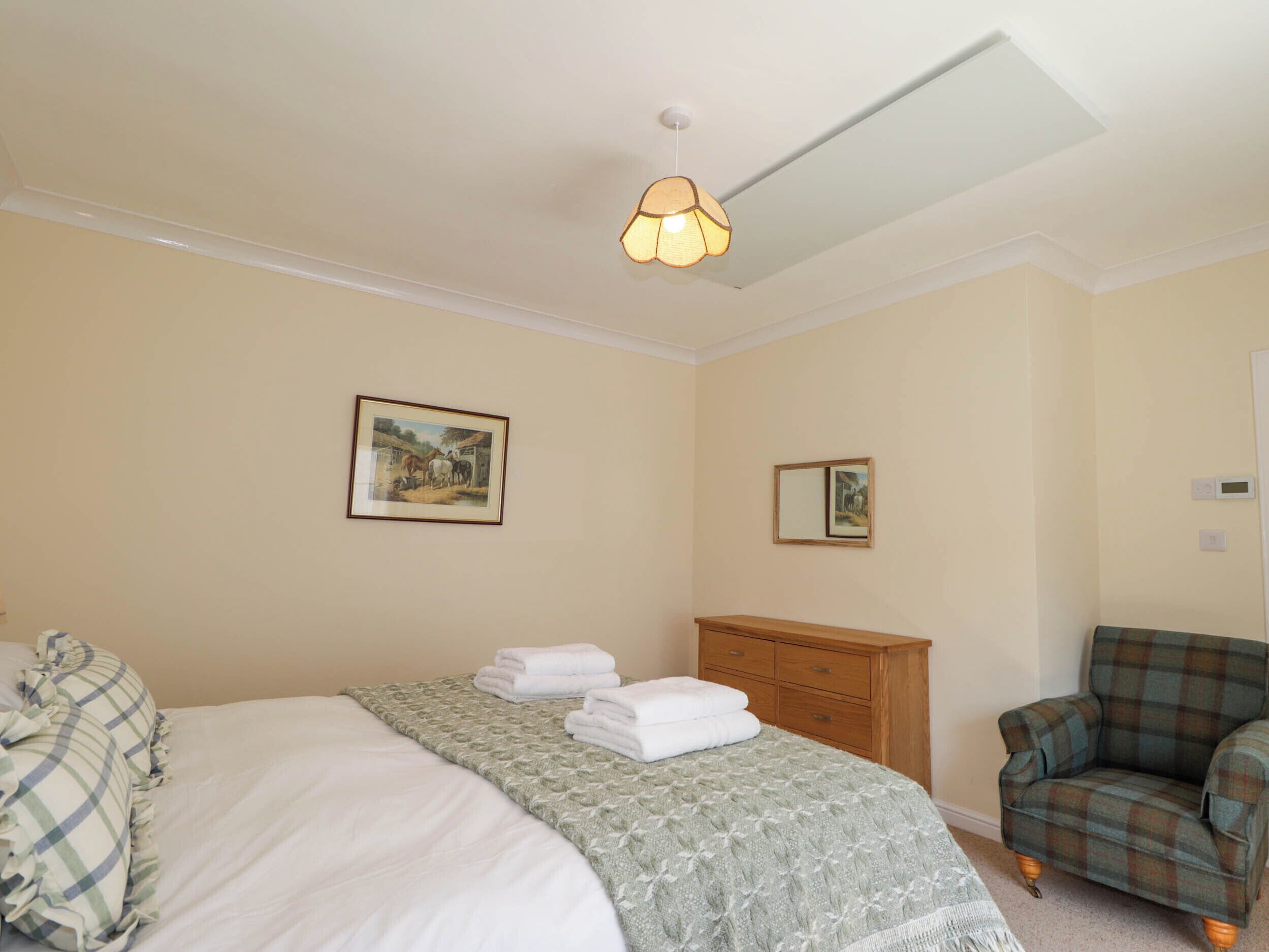 Un dormitorio con una cama, una silla, un aparador y dos cuadros en la pared.