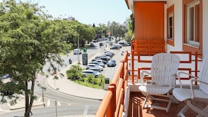 Ein Balkon mit weißen Stühlen mit Blick auf einen Parkplatz und eine Straße.
