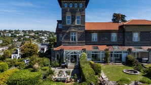 A large stone building with a tower, a covered patio, and a well-maintained garden.