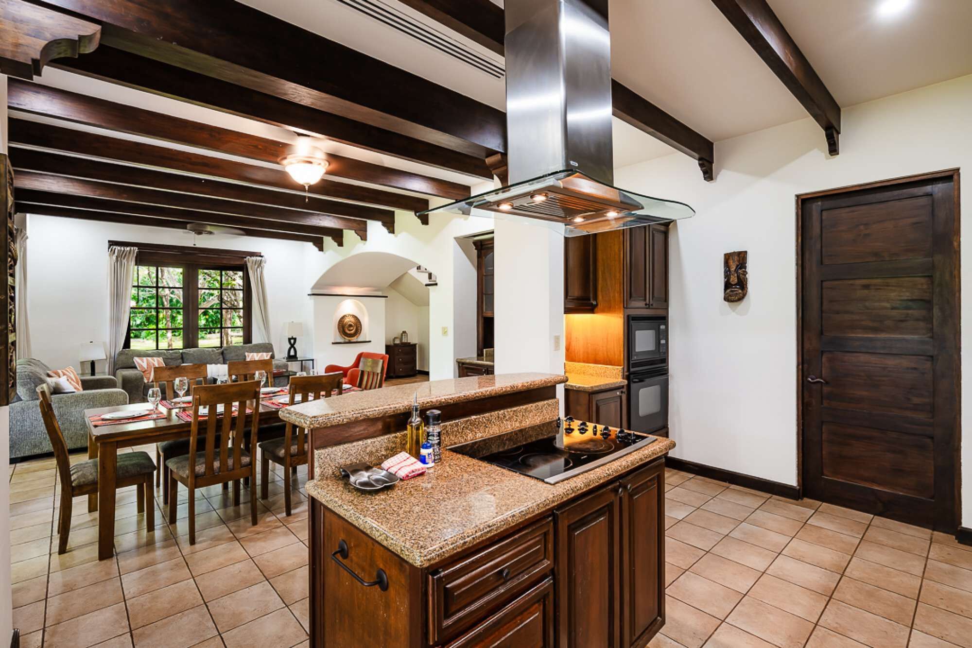 Cozinha com bancadas de granito, coifa de aço inoxidável, armários de madeira e uma área de jantar com mesa e cadeiras.