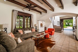 A spacious living room with a sofa, armchairs, a coffee table, and a cowhide rug. A staircase leads to an outdoor area.
