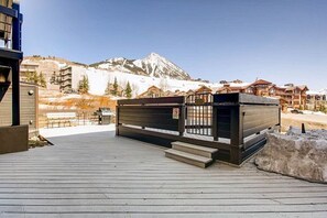 Une terrasse en bois avec un petit bâtiment, une montagne en arrière-plan et un ciel dégagé.