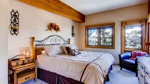 A bedroom with a wooden headboard bed, a nightstand with a lamp, a dresser, and a window with a view of the outdoors. - Crested Butte Mountain Resort Properties by Vail (Crested Butte)