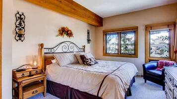 A bedroom with a wooden headboard bed, a nightstand with a lamp, a dresser, and a window with a view of the outdoors.