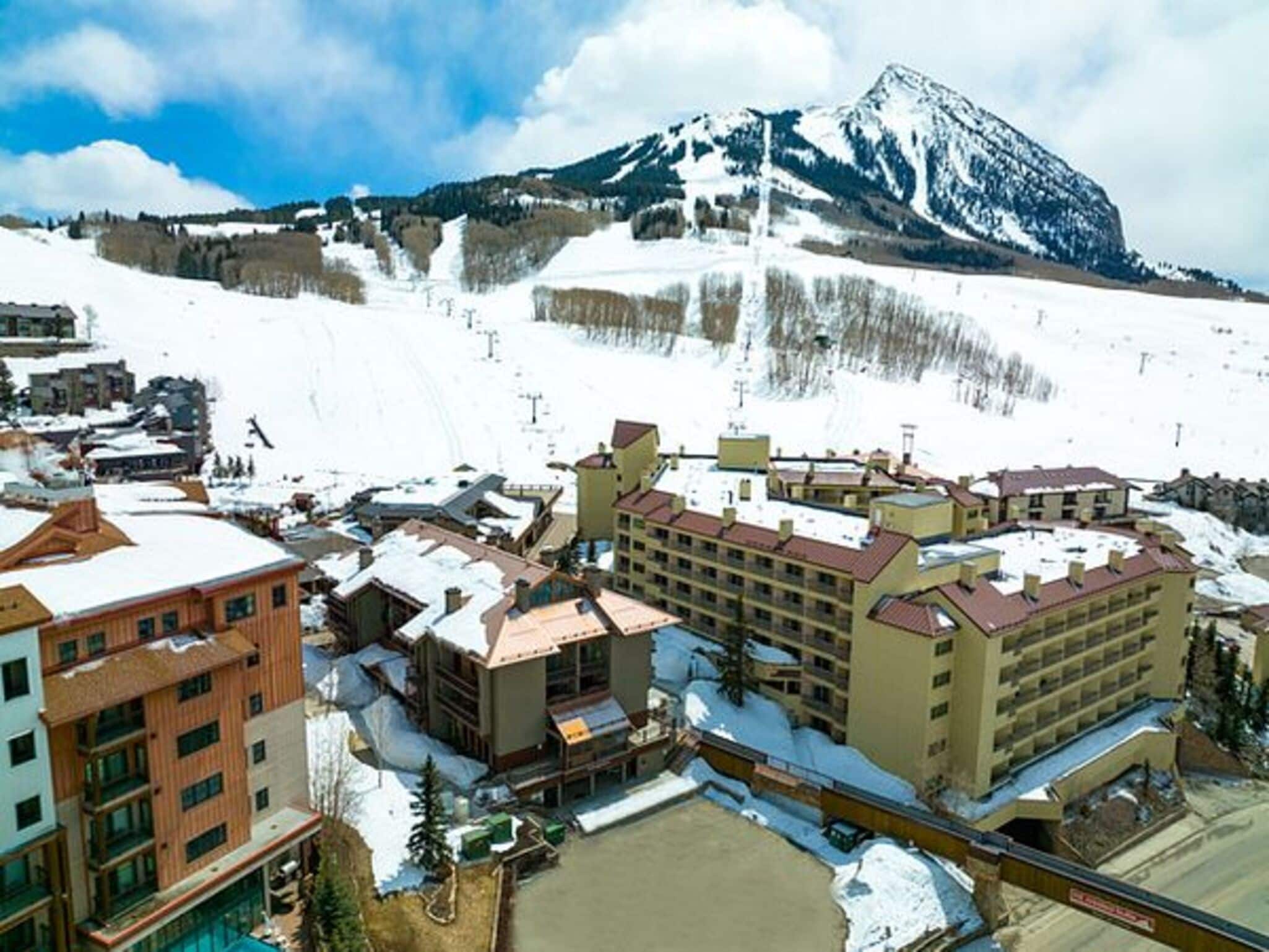 A hotel complex with multiple buildings, a ski slope in the background, and a mountain.