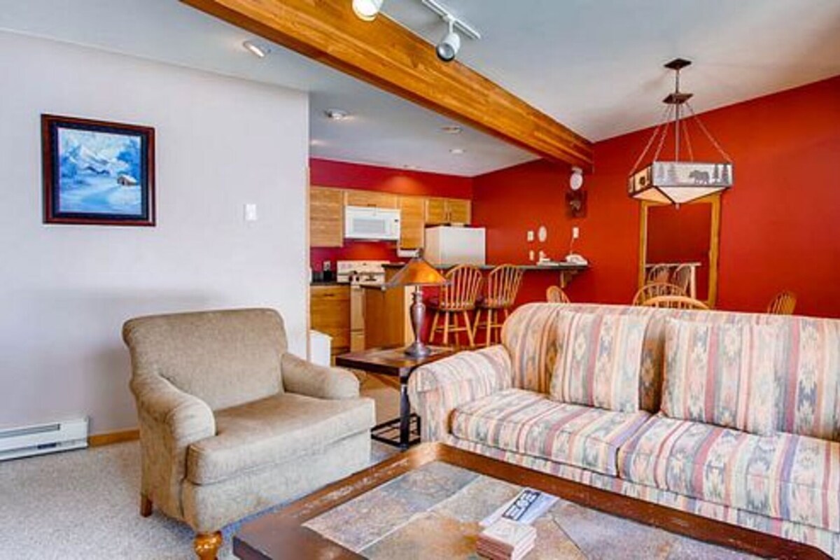 A living room with a sofa, armchair, and a dining area with chairs and a table.