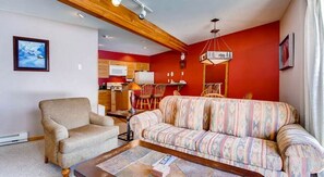 A living room with a sofa, armchair, and a dining area with chairs and a table. - Crested Butte Mountain Resort Properties by Vail (Crested Butte)
