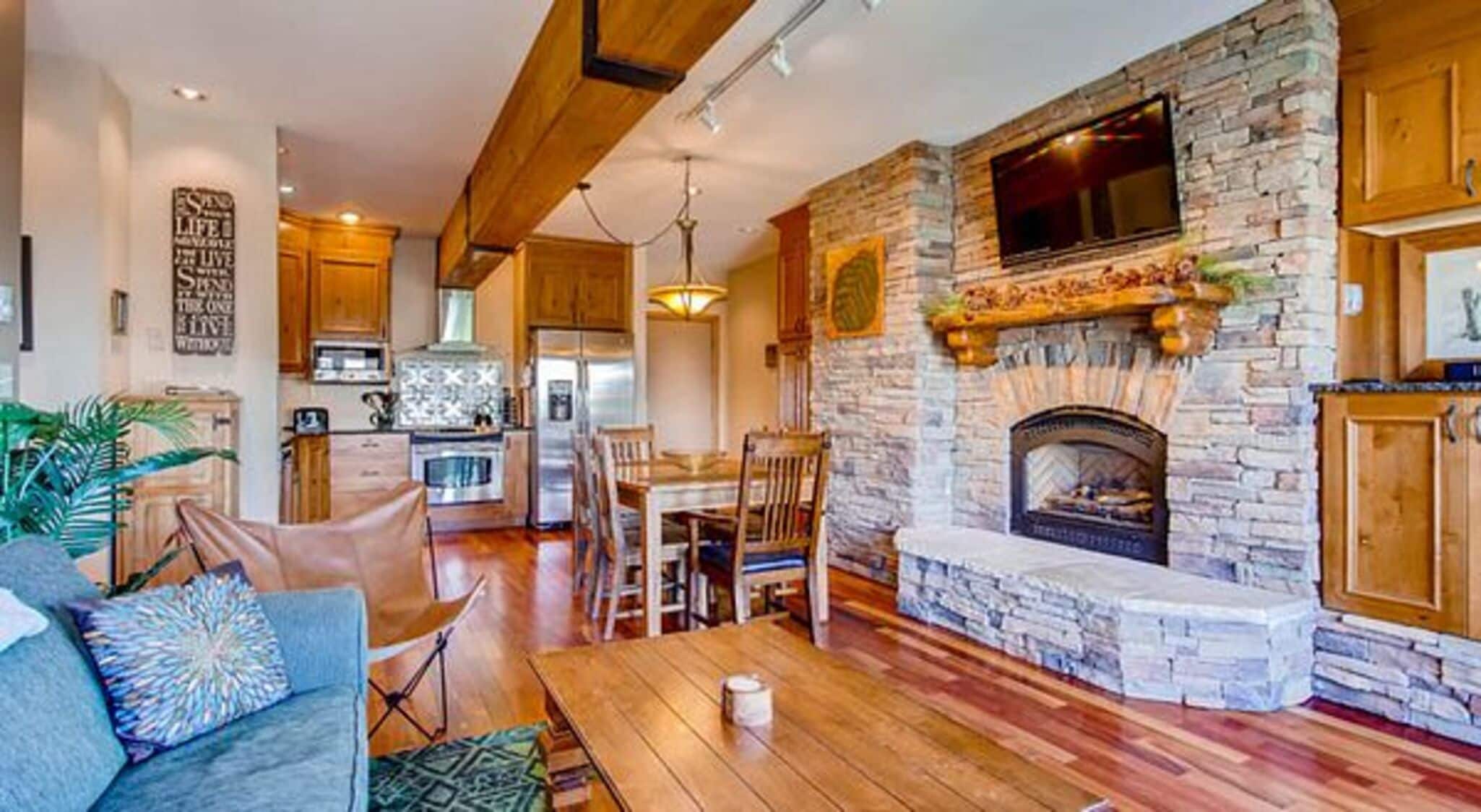 A spacious living room with a stone fireplace, wooden ceiling beams, and a dining area with a table and chairs.