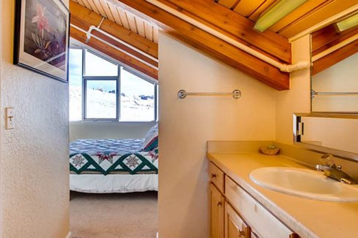 Une chambre à coucher avec un lit, une fenêtre et une salle de bain équipée d’un lavabo et d’un miroir.