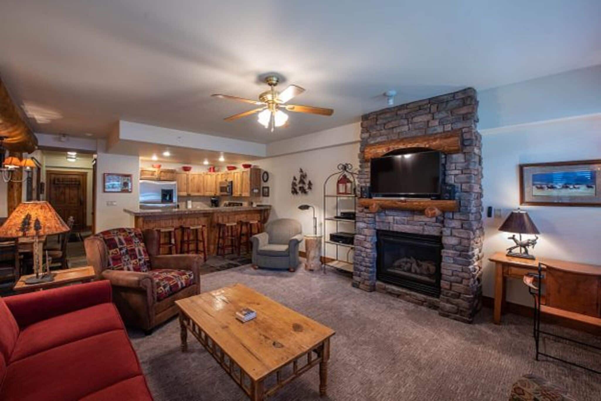 A cozy living room with a fireplace, a television, and a kitchen area in the background.