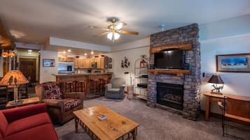 A cozy living room with a fireplace, a television, and a kitchen area in the background.