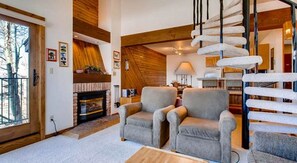 A cozy living room with a fireplace, two armchairs, a wooden ceiling, and a spiral staircase. - Crested Butte Mountain Resort Properties by Vail (Crested Butte)