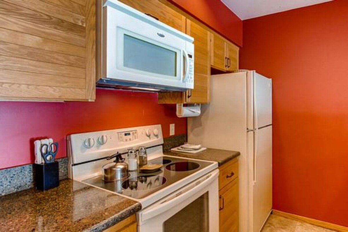 A kitchen with a white stove, oven, microwave, and refrigerator, wooden cabinets, and a red wall.