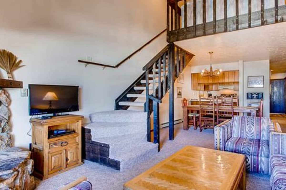 Ein geräumiger Wohnbereich mit Treppe, Fernseher und Essbereich mit Stühlen und Tisch.
