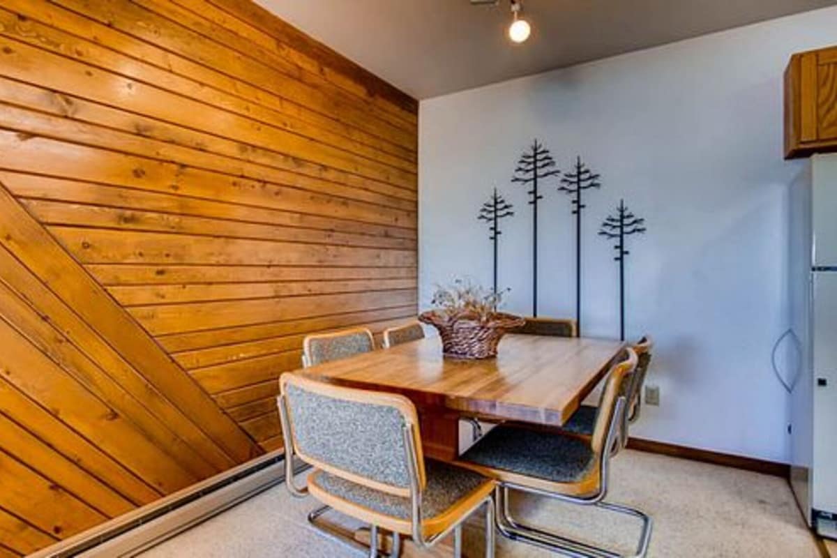 A dining area with a wooden table and chairs, a decorative wall with tree silhouettes, and a white refrigerator.
