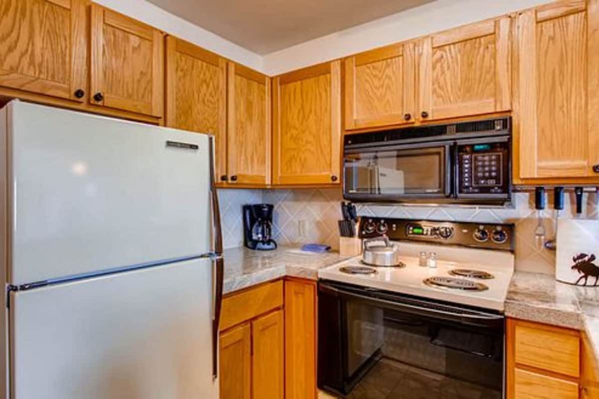 A kitchen with wooden cabinets, a white refrigerator, a microwave, and an oven.