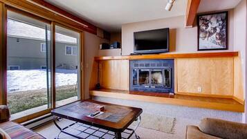 A living room with a fireplace, a television, and a large window overlooking a snowy yard.