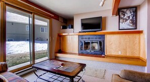 Un salón con chimenea, televisor y un ventanal que da a un patio nevado.
