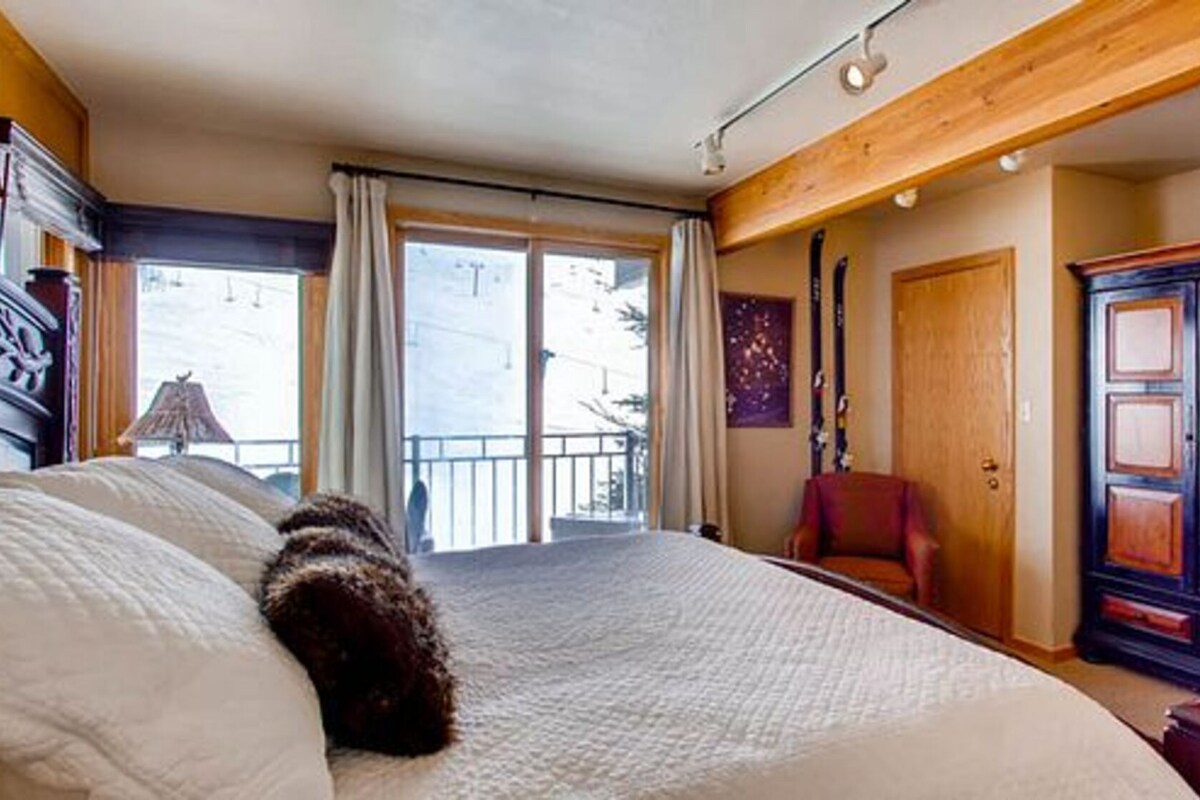 A bedroom with a large bed, a wooden wardrobe, a red chair, and a balcony with curtains.