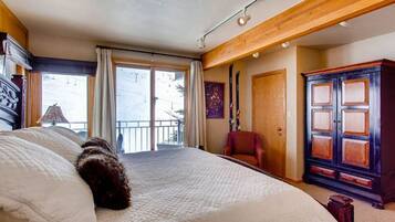 A bedroom with a large bed, a wooden wardrobe, a red chair, and a balcony with curtains.
