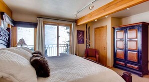 A bedroom with a large bed, a wooden wardrobe, a red chair, and a balcony with curtains. - Crested Butte Mountain Resort Properties by Vail (Crested Butte)