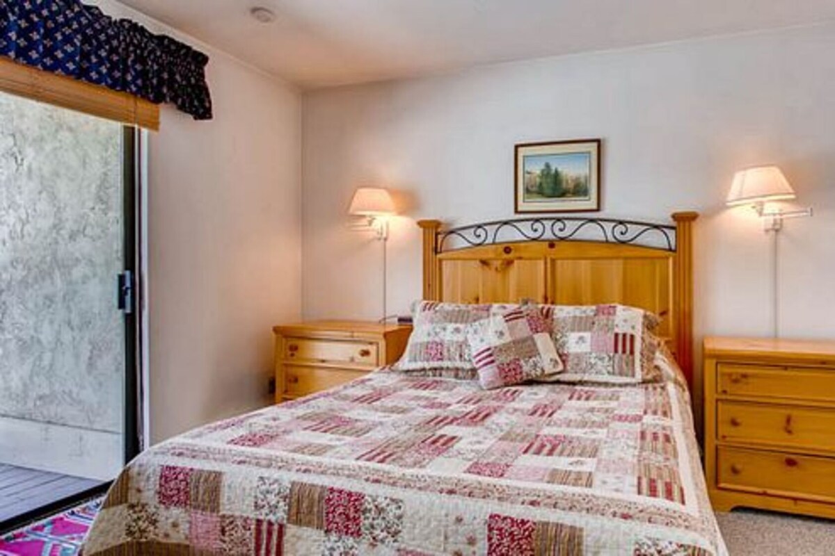 A bedroom with a wooden bed, two bedside tables, a nightstand, a window with a view, and a door.