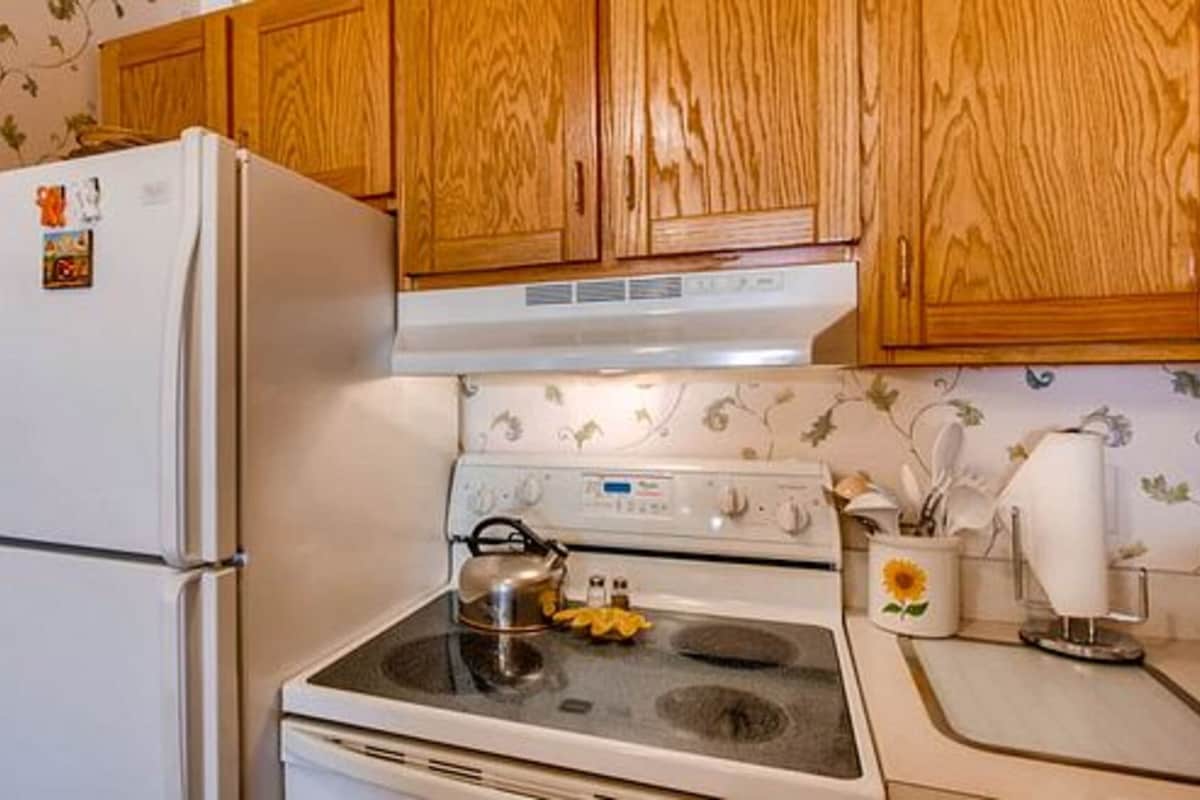 A kitchen with wooden cabinets, a white refrigerator, a stove, and a kettle on the stove.