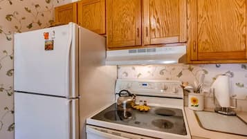 Une cuisine avec des meubles de rangement en bois, un réfrigérateur blanc, une cuisinière et une bouilloire posée sur la cuisinière.