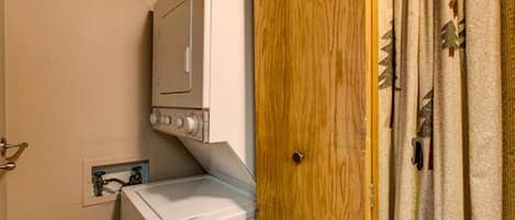 A laundry area with a washing machine and dryer, a wooden door, and a power outlet on the wall.