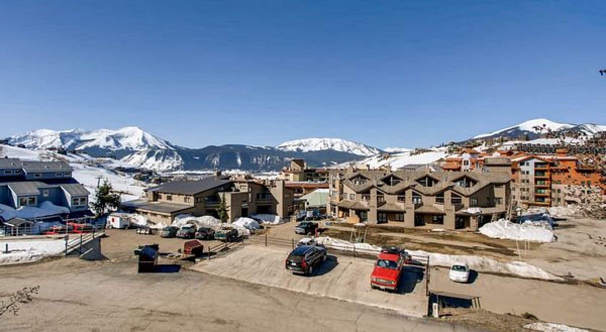 Un hôtel composé de plusieurs bâtiments, avec un parking et des montagnes enneigées en arrière-plan.