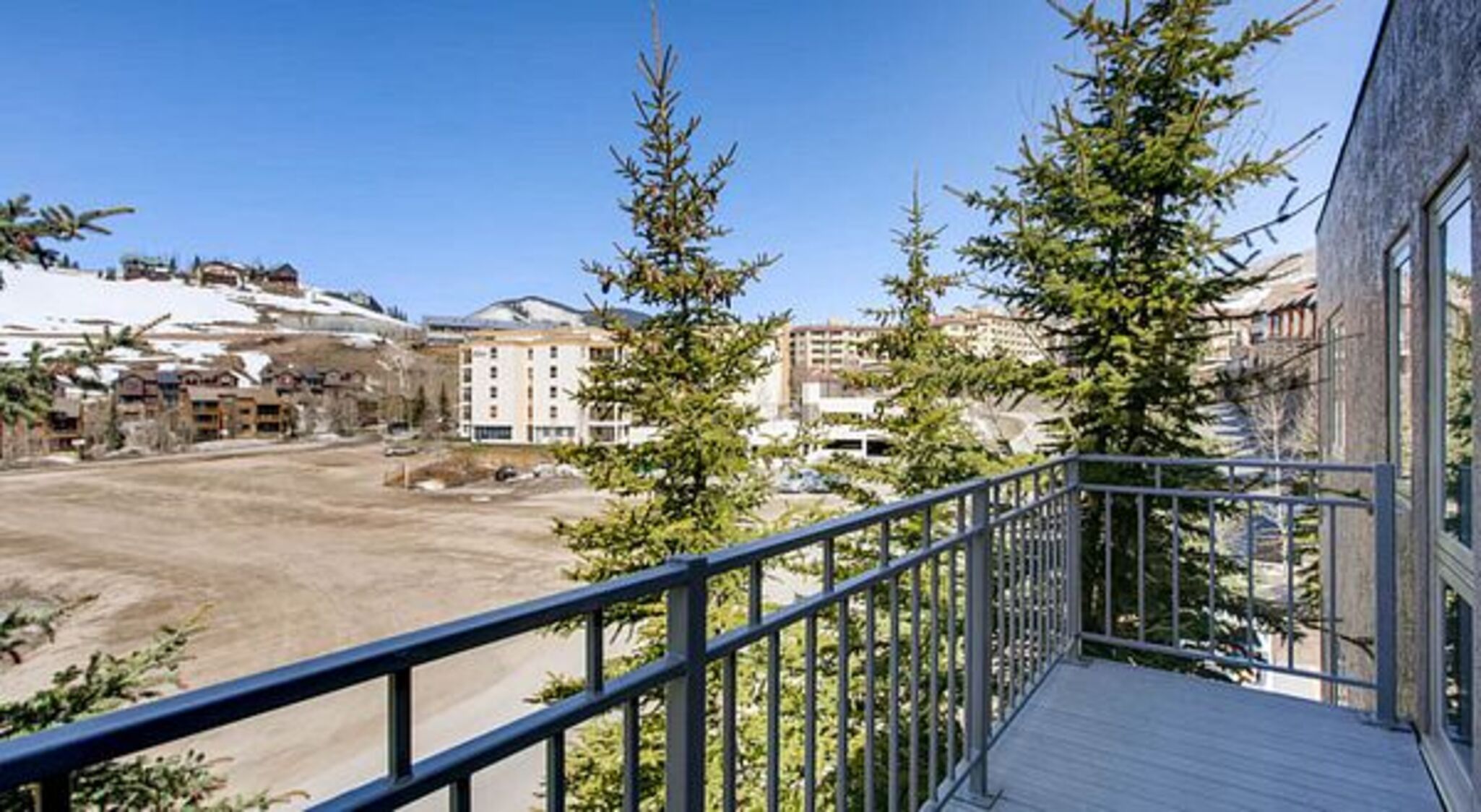 A balcony with a view of a parking lot, buildings, and snow-covered hills.