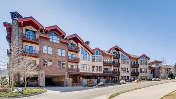 A row of multi-story buildings with balconies, a stone facade, and a clear sky.