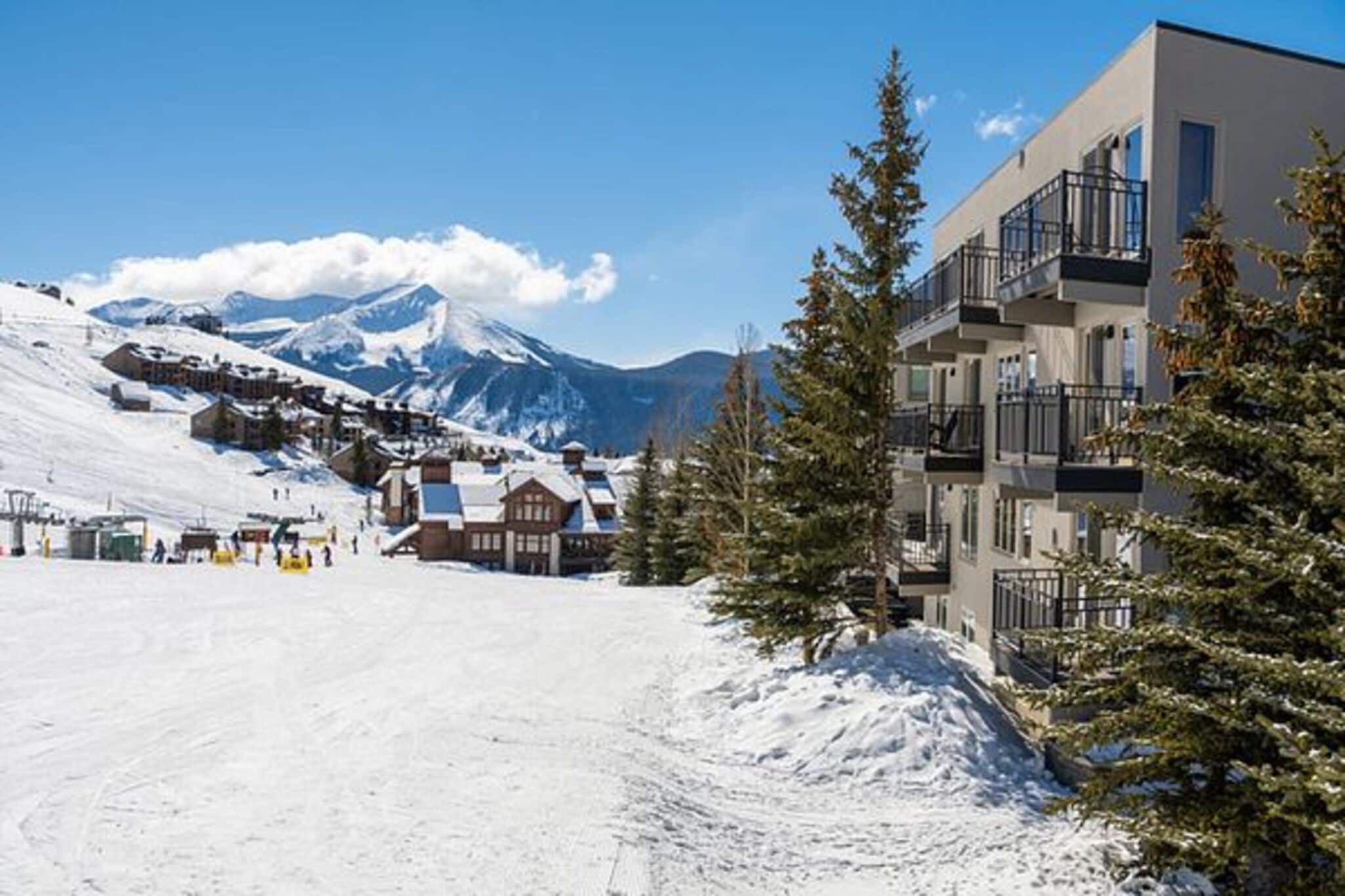 A snow-covered mountain town with modern buildings, a ski slope, and a clear sky.
