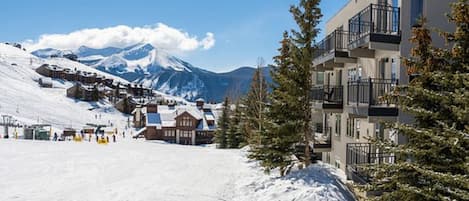 A snow-covered mountain town with modern buildings, a ski slope, and a clear sky.