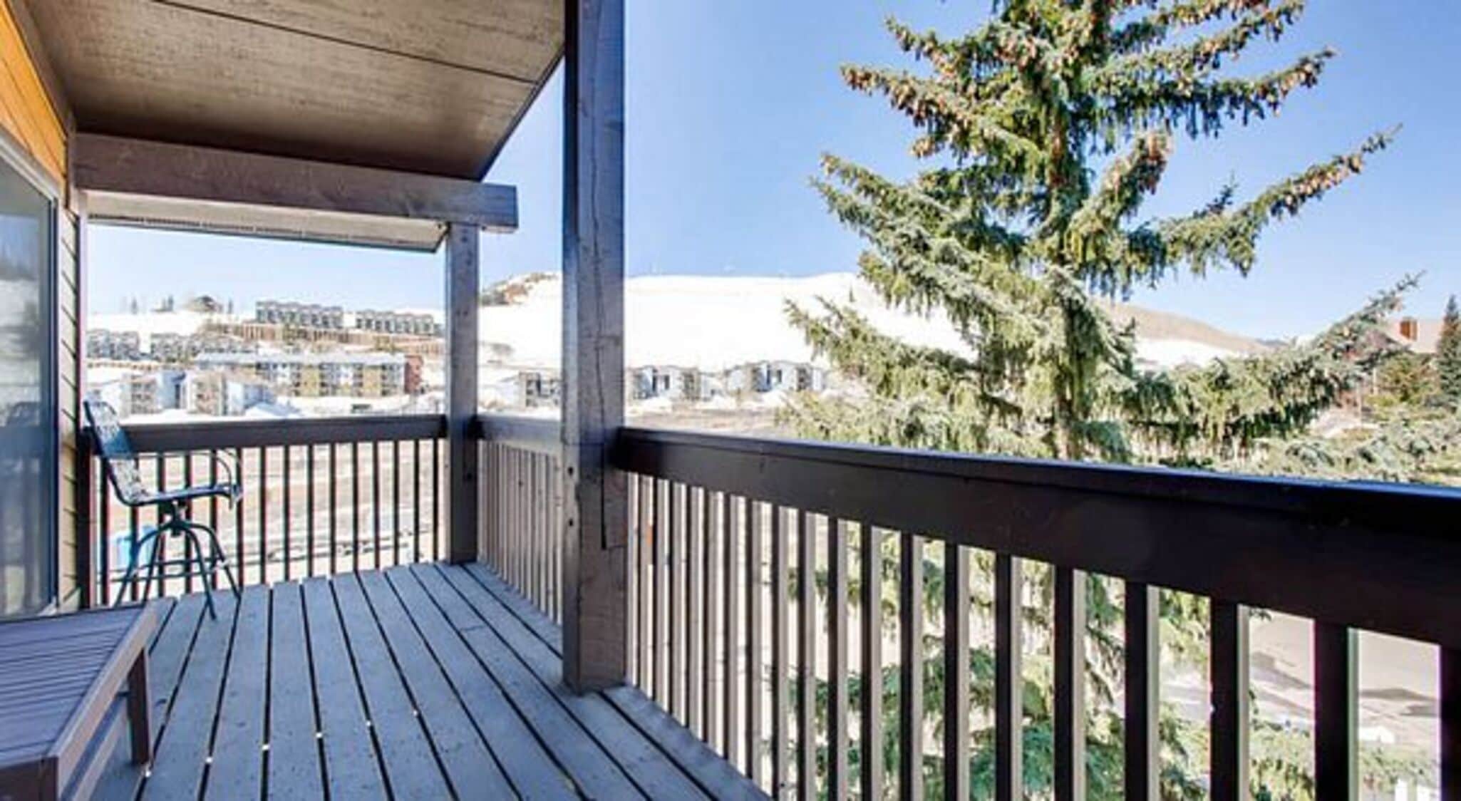 Un balcone in legno con vista su edifici e un conifero.