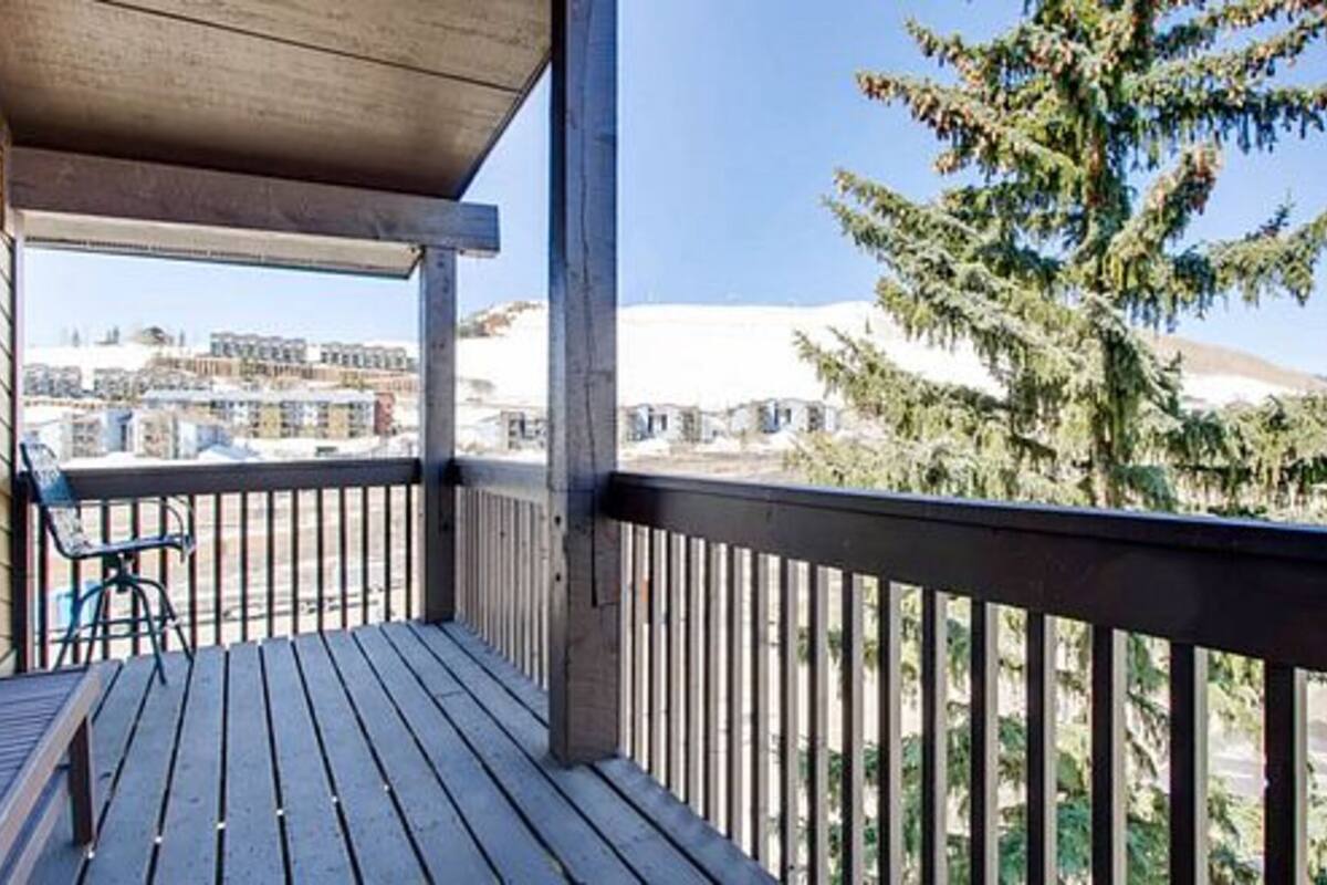 Ein Holzbalkon mit Blick auf Gebäude und einen Nadelbaum.