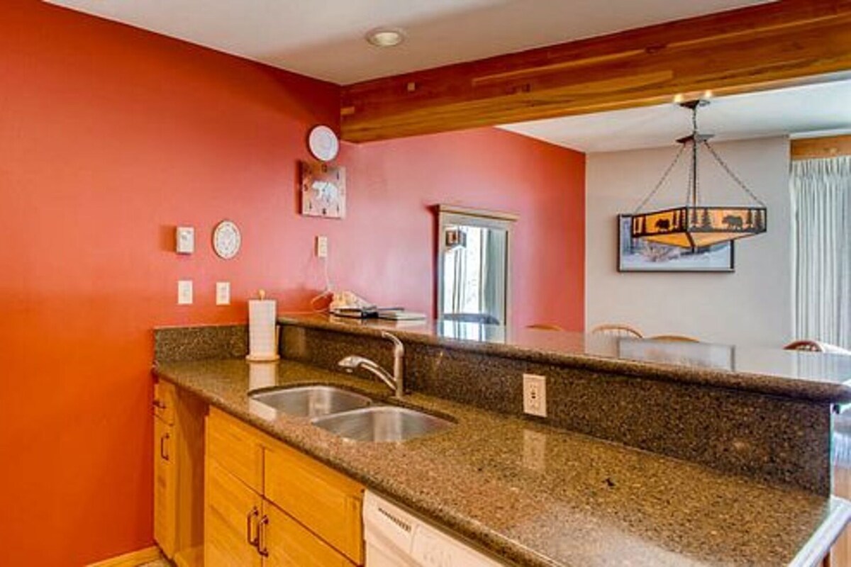 A kitchen with a granite countertop, wooden cabinets, a stainless steel sink, and a red wall.