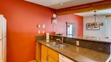 A kitchen with a granite countertop, wooden cabinets, a stainless steel sink, and a red wall.