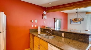 Una cocina con encimera de granito, armarios de madera, pileta de acero inoxidable y pared roja.