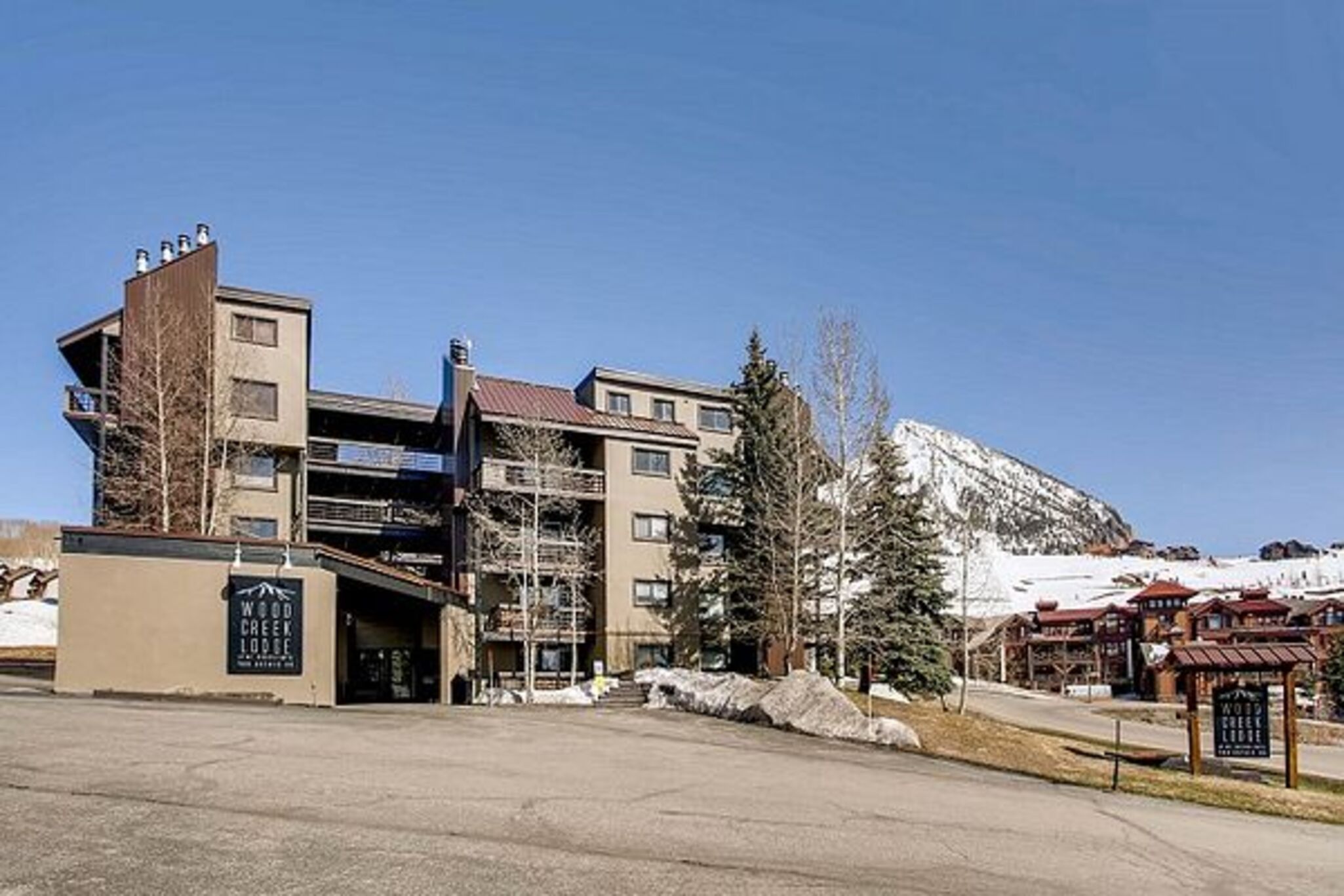 Un hotel de varios pisos con un telesilla al fondo, un estacionamiento y vistas a la montaña.