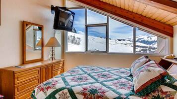 A bedroom with a bed, a dresser, a TV mounted on the wall, and a window with a snowy mountain view.