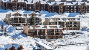 Un complejo turístico cubierto de nieve con varias edificaciones, incluyendo una cabaña y habitaciones de huéspedes, y una pista de esquí al fondo.
